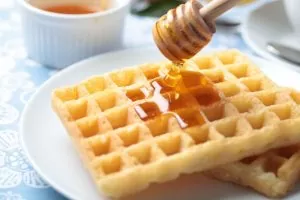 12895362 – pouring honey on belgian waffles using honey dipper