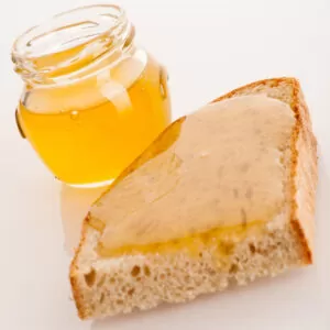 Sweet sticky golden honey on a slice of fresh bread and a glass